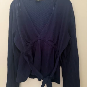 Mörkblå tröja från Gina Tricot - Snygg mörkblå tröja från Gina Tricot i storlek L. Tröjan har långa ärmar, v-ringad hals och ett knytband i midjan som ger en schysst siluett. Materialet är mjukt och har en lätt struktur, passar perfekt till vad som helst. Tröjan köptes ganska nyligen och är knappt använd og priset ligger på 300 spänn men jag säljer den lite billigare då jag inte har någon användning av tröjan.