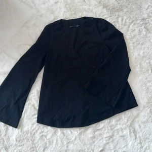 Svart blus  - Säljer en svart blus från lager 157 i storlek S. Blusen har långärmade ärmar och en snygg v-ringad front som ger en stilren look.