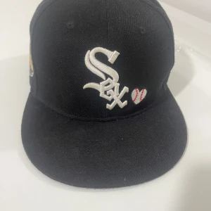 Baseball cap Chicago White Sox 59FIFTY keps New Era - Snygg svart 59FIFTY keps från New Era med Chicago White Sox-logga framtill, broderad baseballhjärta och texten 'Love & Hustle = Game' bak. På sidan finns World Series 2005-märke. Klassisk rak skärm och äkta MLB-merch.
