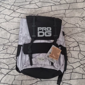 PRO DG ryggsäck med camomönster - Säljer en snygg ryggsäck från PRO DG i grått och svart camouflagemönster. Väskan har flera fickor med spännen, vadderade axelremmar och USB-port för laddning. Perfekt för laptop och vardagsäventyr. Slitstarkt syntetmaterial och cool urban look.