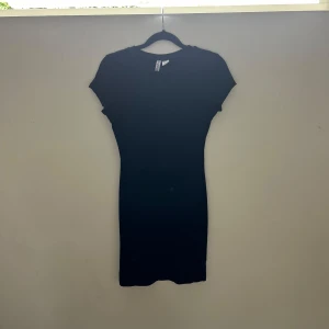 Svart ribbad kortklänning H&M Divided - Säljer en svart ribbad kortklänning från H&M Divided i storlek S. Klänningen har rund hals, korta ärmar och en slim passform som sitter snyggt mot kroppen. Perfekt för dig som gillar enkel och stilren design med lite edge.