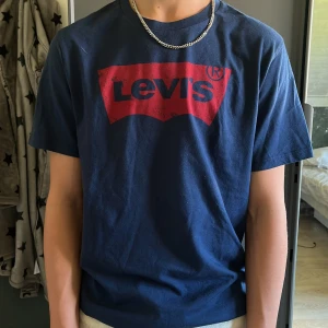 Mörkblå Levi's t-shirt med röd logga - Snygg mörkblå t-shirt från Levi's i bomull med klassisk röd logga framtill. Modellen är normal passform och har korta ärmar. Perfekt för dig som gillar stilrena och ikoniska plagg med streetkänsla.