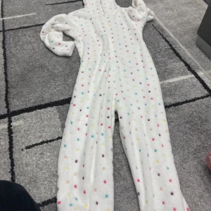 Vit fleecehoodie med färgglada prickar - Supermysig vit hoodie i fleece med huva och dragkedja hela vägen. Prickigt mönster i olika färger som rosa, blå, gul och brun. Perfekt för chill hemma eller när du vill vara extra bekväm. Långärmad och med sköna muddar vid ärmarna.