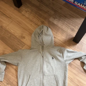 Ralph Lauren Zip Hoodie - En grå zip hoodie från Ralph Lauren i mycket gott skick, säljes endast då jag tänkte prova en annan stil :)
