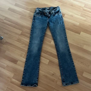 Blå bootcut jeans low rise 27/32 - Snygga blå jeans med bootcut och låg midja. Jeansen har klassisk femficksdesign och är tillverkade i ett slitstarkt denimtyg. Perfekta för dig som gillar en avslappnad men ändå trendig look.