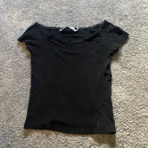 Svart topp med spets från 157, XS - Svart kortärmad topp från 157 i storlek XS. Toppen har en söt spetskant runt halsringningen och ärmarna, vilket ger en extra detalj. Modellen är figurnära och passar perfekt till jeans eller kjol. Mjuk och skön bomullskänsla.