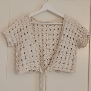 Beige stickad bolerotopp med knyt - Superfin beige bolerotopp i stickat material med korta ärmar och knyt framtill. Toppen har ett hålmönster över hela och är croppad i modellen. Perfekt att slänga över ett linne eller klänning💕 passar XS/S
