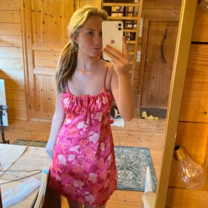 Rosa blommig kortklänning med snörning - Superfin rosa kortklänning med blommigt mönster och tunna axelband. Klänningen har snörning vid bysten och en figurnära passform. Perfekt för sommarens alla tillfällen och ger en färgglad och fräsch vibe.