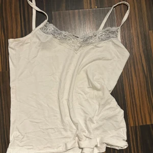 Vit spetslinnetopp från 157 Black Label - Supersöt vit linnetopp med tunna axelband och v-ringning dekorerad med spets. Perfekt för lager-på-lager eller till kjol och jeans. Mjuk och lätt i bomullsmix, enkel att styla för en chill look.