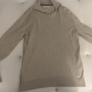 Beige half zip tröja Jack & Jones - Beige långärmad tröja från Jack & Jones med half zip-dragkedja och hög krage. Tröjan är ribbad vid ärmslut och nederkant, vilket ger en clean och stilren look. Perfekt för lager-på-lager och chill vardagsstil.