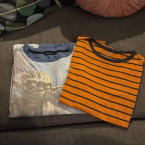 2 t-shirts: Yoda & orange randig - Två t-shirts i cool stil. Ena har ett stort Yoda-tryck på ljusblå botten, perfekt för Star Wars-fans. Den andra är orange med marinblå ränder och rund hals. Båda är kortärmade och i mjuk bomull. Snygga att matcha med jeans eller shorts.