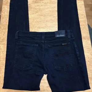 Svarta skinny jeans från Nudie Jeans - Snygga svarta skinny jeans från Nudie Jeans, tillverkade i 100% ekologisk bomull. Klassisk femficksmodell med svarta sömmar och diskret logga på bakfickan. Perfekta för dig som gillar en slimmad passform och stilren look.