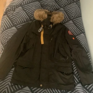 Parajumpers vinterjacka man  - Säljer en svart vinterjacka från Parajumpers med gul detalj vid halsen. Jackan har flera fickor, dragkedja och knappar framtill samt patch på ärmen. Perfekt för kalla dagar och riktigt stilren look. Storleken är medium VID SNABB AFFÄR KAN PRISET DISKUTERAS 