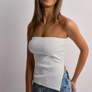 Vit ribbad bandeau tubtopp Nelly - Säljer en stilren vit bandeau tubtopp med ribbad struktur. Toppen är ärmlös och axelbandslös, med en rak och enkel passform samt slits i sidorna. Perfekt för dig som gillar minimalistisk och clean stil. Lappen kvar🩷