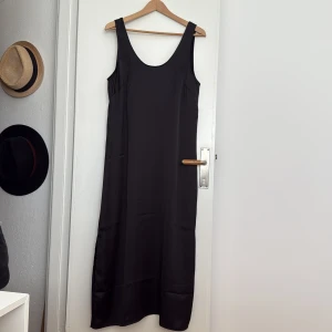 Svart långklänning i satin från HM - Svart långklänning i satin med breda axelband och rundad urringning fram och bak. Rak modell med slitsar i sidorna. 