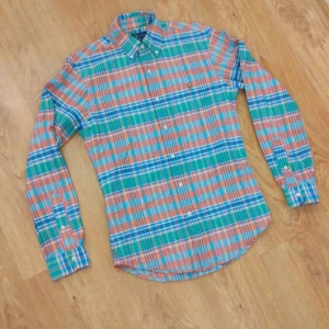 Rutig skjorta från Ralph Lauren S - Färgglad rutig skjorta från Ralph Lauren i slim fit. Skjortan har långa ärmar, klassisk krage och knäppning framtill. Mönstret är i grönt, blått, orange och vitt. Broderad logga på bröstet. Perfekt för dig som gillar preppy stil.