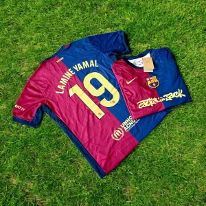 FC Barcelona Lamine Yamal tröja Nike - Snygg FC Barcelona matchtröja med Lamine Yamal och nummer 19 på ryggen. Tröjan är kortärmad och har klassiska blå och vinröda fält, guldiga detaljer och klubbmärke på bröstet. Tillverkad i lätt och ventilerande material, perfekt för fotbollsplanen.