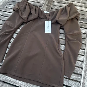 Brun offshoulder topp från NA-KD - Säljer en brun offshoulder topp från NA-KD med långa ärmar och snygg rynkad detalj vid axlarna. Toppen har en smickrande passform och är perfekt för dig som vill sticka ut med en trendig look. Materialet känns mjukt och följsamt. Fick den utan ett av banden men går utmärkt att ha på utan då det är silikon runt om