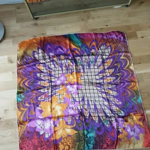 Färgglad blommig silk halsduk från Sabar - Stor och mjuk silke halsduk från Sabar med blommigt mönster i lila, orange och gult. Sidenliknande material med coola vågiga detaljer och rutigt inslag i mitten. 90×90cm