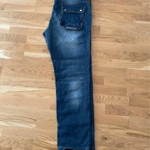 Säljer nya jeans – 120 kr👖 Jeans i storlek 38✅ Helt nya, 💰 Pris: 120kr - Säljer ett par blå jeans med snygg tvätt och en stor ficka med lock och knappar bak. Jeansen har raka ben och klassisk passform, perfekta för en avslappnad stil. Materialet är jeans och färgen är en mellanblå ton med lätt slitning.Säljer nya jeans – 120 kr  👖 Jeans i storlek 38 ✅ Helt nya,   💰 Pris: 120kr