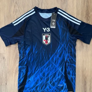 Japan Y-3, Adidas Fotbollströja - Japan landslagströja i samarbete med Y-3 och Adidas. Marinblå med blå grafiskt mönster, vita ränder på axlarna och JFA-emblem på bröstet. Tillverkad i lätt funktionsmaterial (AEROREADY) och har korta ärmar. Slim fit-modell.                          Japan 🇯🇵 Landslag 2024/2025 Tröja, Storlek Herr S, aldrig använd med lappen kvar.