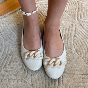 Vita ballerinaskor med kedjedetalj - Snygga vita ballerinaskor från Alley med rund tå och en chunky kedjedetalj framtill. Skorna har platt sula och är tillverkade i syntetmaterial. Perfekta för dig som gillar en clean och stilren look med en twist.