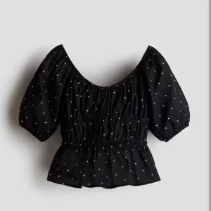 Svart prickig blus  - Supersöt svart blus med små vita prickar och puffiga trekvartsärmar. Modellen har smock i midjan och en lätt volang nertill för en feminin look. Perfekt att styla med jeans eller kjol för en trendig outfit. Inga returer