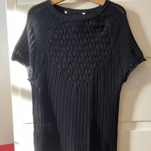 Svart stickad kortärmad topp - Snygg svart stickad spets topp med korta ärmar och ett genombrutet mönster upptill. Toppen är ribbad nertill och har en rund halsringning. Perfekt att styla med jeans eller kjol för en trendig look. Lappen är avklippt då man hade sett den i ryggen annars. 