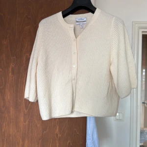 Krämvit kofta i merinoull från & Other Stories - Superfin krämvit kofta från & Other Stories i 100% merinoull. Kortare modell med ribbstickat material, rund hals och knappar framtill. 