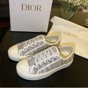 Dior Oblique (walk’n dior) i grått och vitt - Snygga Dior Oblique sneakers i grått och vitt med klassiskt monogrammönster. Skorna har rund tå, platt sula och vita snören med 'Christian Dior' tryckt på. Tillverkade i canvas med detaljer i skinn och gummisula. Perfekta för dig som vill ha en lyxig och trendig look.Allt og finns kvar