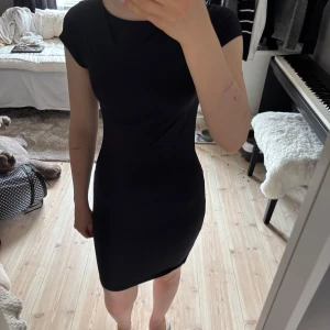Svart tight kortklänning - Enkel och stilren svart kortklänning med tight passform och korta ärmar. Klänningen har rund halsringning och är gjord i ett mjukt, stretchigt material som sitter snyggt på kroppen. Perfekt för dig som gillar minimalistisk och clean stil.