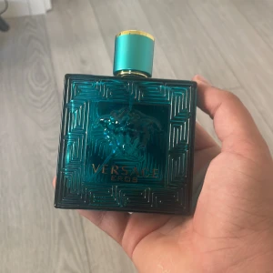 Tom flaska - Versace Eros parfym i en stilren, turkosblå glasflaska med guldiga detaljer och Medusa-huvudet på både flaska och lock. Flaskan har en fyrkantig form med grekiskt mönster och känns riktigt lyxig och ikonisk.