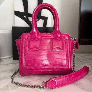 Rosa väska från Zara - Snygg handväska från Zara.Väskan har både handtag och en avtagbar axelrem i silverkedja. Stängs med dragkedja och har svart innerfoder. Nästintill oanvänd och mycket bra skick. Obs liten skavank, se bild 4.