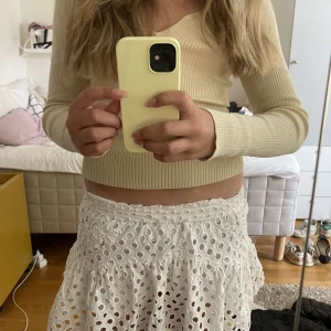 Vit broderad kortkjol från Zara - Superfin vit kortkjol från Zara med broderade detaljer och hålmönster. Kjolen har volanger och resår i midjan för en bekväm passform. Perfekt för varma dagar och ger en söt och fräsch look. Fodrad på insidan så den inte blir genomskinlig.