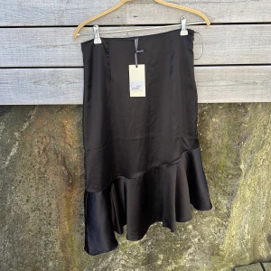 Svart volangkjol By Malina M - Supersnygg svart kjol från By Malina i modellen Ellie skirt. Kjolen  är i en glansig, mjuk satinliknande kvalitet. Perfekt för fest eller bara snygghet 🤗 KÖPT FÖR 1499kr och ej provad eller använd 