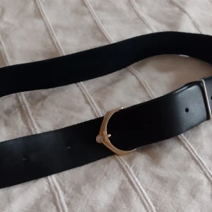Svart skärp i äkta skinn  med guldfärgat spänne och "diamant"  - Stilrent svart bälte i äkta skinn med ett unikt guldfärgat spänne som har en liten glittrande "diamant". Ca 3,8 cm brett och 100 cm långt. Bältet har klassiska hål för justering. Har bara använts ett par gånger och är i fint skick ✨