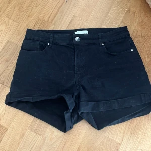 Svarta jeansshorts från H&M - Svarta jeansshorts från H&M med klassisk femficksdesign och uppvikta benslut. Shortsen har bälteshällor och knappstängning framtill. Perfekta för en chill sommardag och enkla att matcha med allt.🥰