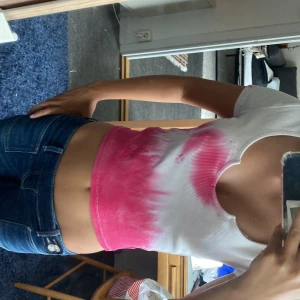 Vit och rosa ribbad croppad topp - Superfin croppad topp från Bik Bok i ribbat material. T-shirten är vit med rosa tie-dye effekt och har en snygg v-ringning med liten notch. Kortärmad och figurnära passform, perfekt till jeans eller kjol för en cool look.