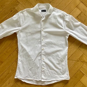 Vit slim fit skjorta Tiger of Sweden - Klassisk vit skjorta från Tiger of Sweden i slim fit-modell. Skjortan har långa ärmar, knappar framtill och en stilren krage. Tillverkad i bomull för en skön och fräsch känsla. Perfekt för dig som gillar en clean och tidlös look.