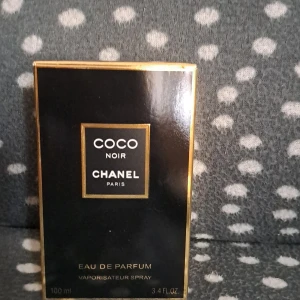 Chanel Coco Noir Eau de Parfum 100ml - Lyxig parfym från Chanel, Coco Noir Eau de Parfum i 100 ml flaska. Flaskan är elegant svart med guldiga detaljer och klassisk fyrkantig form. Kommer med originalkartong i svart och guld. Perfekt för dig som gillar exklusiva och sofistikerade dofter.