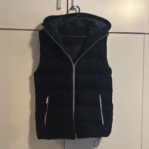 Vendiera väst  - Säljer en marinblå väst från vendiera med huva och hel dragkedja framtill. Västen har två snedställda fickor med dragkedjor och quiltad design. Materialet är manchester vilket ger en snygg struktur. Perfekt för lager-på-lager under kyliga dagar. Passar om du är runt 50-65kg 165-175 för att man kan anpassa med snören längst ner