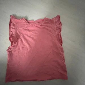 Rosa ärmlös topp från 157 - Säljer en enkel och snygg rosa topp från 157 i storlek S. Toppen är ärmlös med lätt volang vid axlarna och har en rund halsringning. Perfekt för en chill och avslappnad stil.