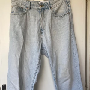 Ljusblå jeans från Bershka - Säljer ett par ljusblå raka jeans från Bershka med klassisk femficksdesign och knappgylf. Jeansen har en loose fit och raka ben, tillverkade i bomull. Perfekta för en avslappnad och trendig look. Fläck på låret se bild