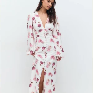 Vit blommig långklänning med slits - Superfin långklänning i vitt med rosa blommor, djup v-ringning och långa ärmar. Klänningen har knappar framtill och en snygg slits. Perfekt för sommarens alla tillfällen! Använd endast en gång ❤️hör av dig för bilder!!