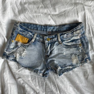 Blå lågmidjade jeansshorts  - Snygga blå jeansshorts, låg midja och coola slitna detaljer. Köpta på second hand med prislappen kvar. Står inte storlek men skulle säga att de passar en XS/S.
