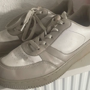 Vita sneakers i skinn med beige detaljer - Snygga vita sneakers med beige detaljer och klassisk snörning. Skorna har en platt sula och är tillverkade i skinn med textilfoder. Perfekta för dig som gillar en clean och stilren look. Passar till det mesta och är riktigt bekväma.