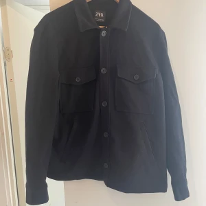 Svart overshirt från Zara i ullmix - Stilren svart overshirt från Zara i ullmix med klassisk krage, stora bröstfickor med lock och knappar framtill. 
