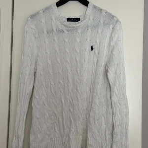 Vit stickad tröja från Ralph Lauren - Säljer en klassisk vit stickad tröja från Ralph Lauren med kabelstickat mönster och broderad logga på bröstet. Tröjan har rund halsringning och långa ärmar. Perfekt för en stilren och tidlös look.