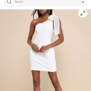 Vit one shoulder klänning från Lulus - Säljer en vit klänning från Lulus med one shoulder och rosett/band på axeln. Klänningen har en figurnära passform och är tillverkad i ett blommigt tyg. Perfekt för student eller sommarens fester!