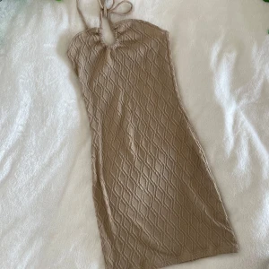 Beige ribbad halterneckklänning från H&M - Säljer en beige/brun ribbad halterneckklänning från h&m. Klänningen har ett snyggt strukturmönster, knytning i nacken och en kroppsnära passform. Perfekt för dig som gillar stilrena och trendiga plagg. Längd: 59cm, Midja: 27cm
